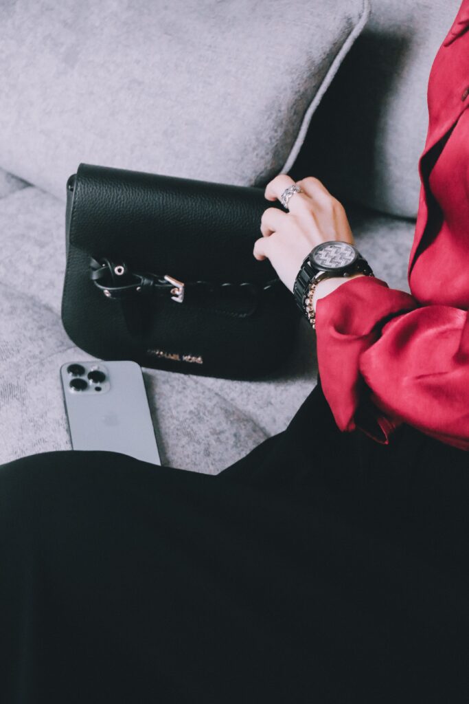 Woman in red attire sitting with a black leather handbag and smartphone.