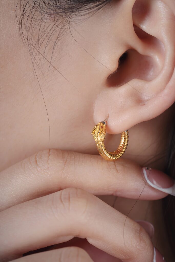 Detailed closeup of a gold hoop earring, showcasing intricate design on an adult woman's ear.