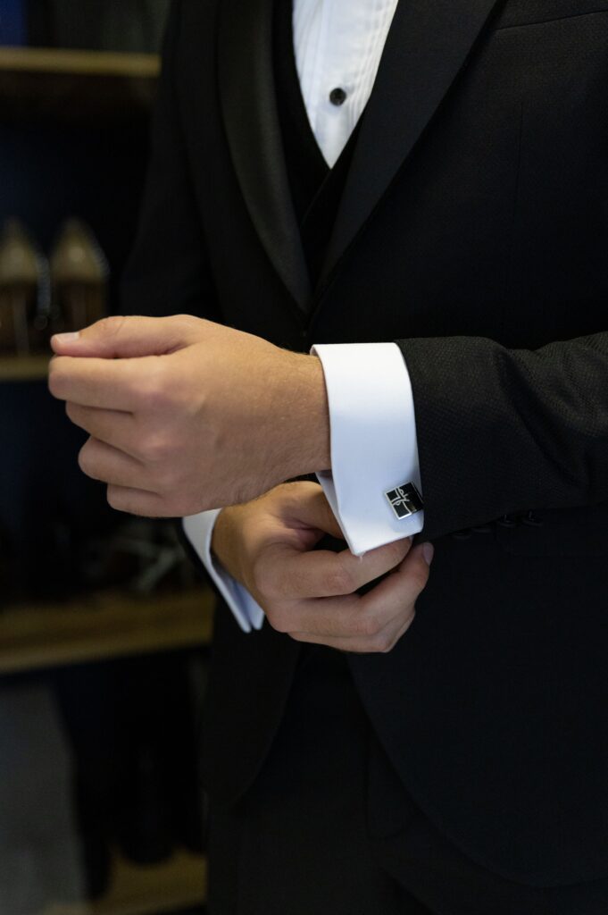 Close-up of a man in formal attire adjusting his cufflinks, emphasizing elegance and preparation.