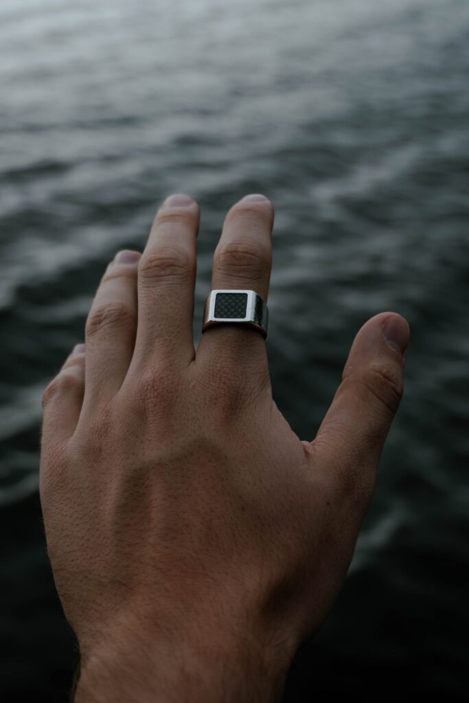 A hand with a silver ring reaches out over waterfront, capturing summer vibes.