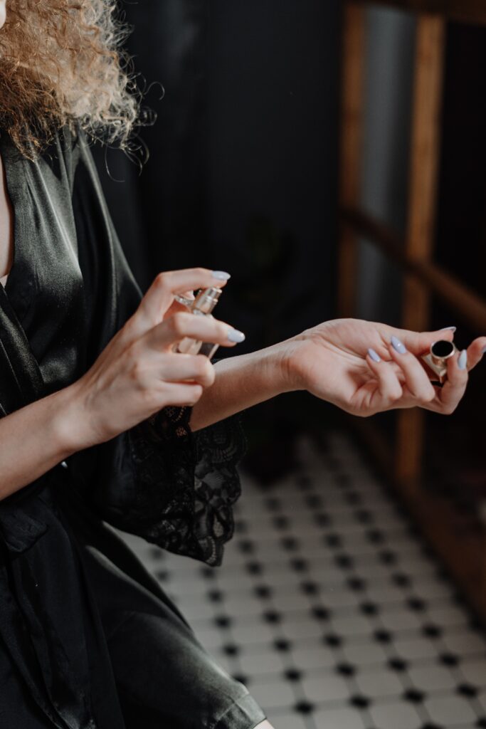 Woman in a dark silk robe delicately applying perfume to her wrist indoors.